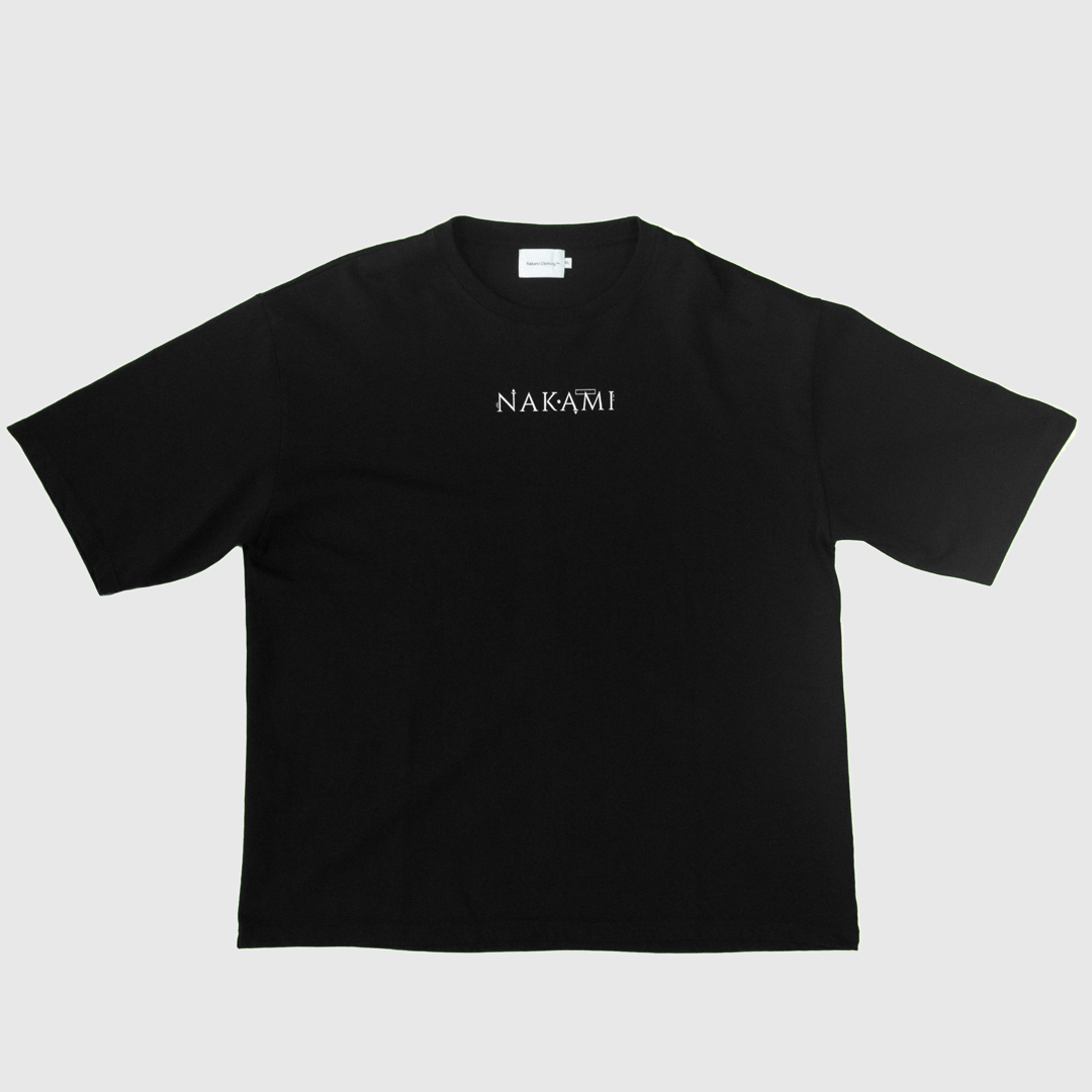 Das schwarze Infinity Shirt von Nakami liegt auf dem Boden. Auf dem Shirt ist das Nakami Logo abgedruckt.