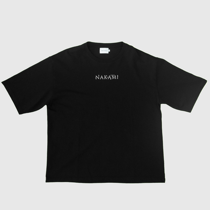 Das schwarze Infinity Shirt von Nakami liegt auf dem Boden. Auf dem Shirt ist das Nakami Logo abgedruckt.