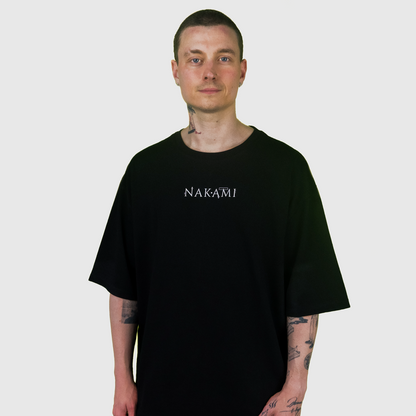 Ein Mann mit kurzen Haaren trägt das schwarze Infinity Shirt von Nakami. Das Model schaut in die Kamera